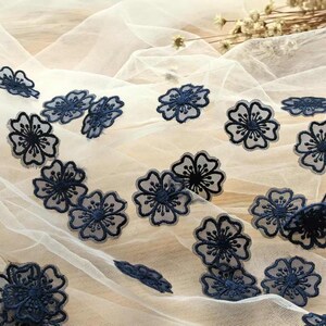 May include: White sheer fabric with navy blue embroidered floral designs. The fabric has a delicate, airy feel.