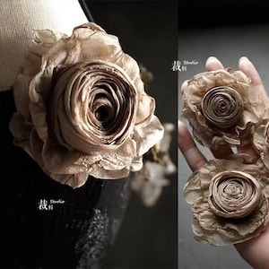 Puede incluir: Primer plano de varias flores de tela en color beige neutro. Las flores tienen un diseño de pétalos en capas, con un centro enrollado. Las flores probablemente están hechas a mano y podrían usarse para varios proyectos de manualidades o como acentos decorativos.