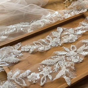 Può includere: Bordino di pizzo bianco perlato con motivi floreali e paillettes. Il pizzo è delicato e intricato, perfetto per aggiungere un tocco di eleganza a qualsiasi progetto.