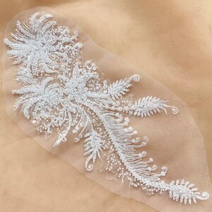May include: White beaded and sequined lace applique with a floral design. The applique is on a sheer white mesh fabric.