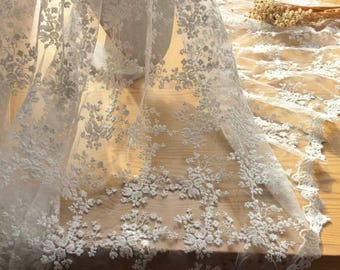 May include: A sheer white fabric featuring intricate floral embroidery and scalloped edges. The delicate lace material displays a dense pattern of small flowers and leaves, creating a textured surface with a semi-transparent quality throughout.
