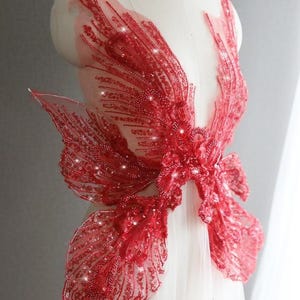 Puede incluir: Aplique de encaje rojo con cuentas con un diseño de mariposa. El aplique está hecho de lentejuelas y cuentas sobre una tela de malla transparente.