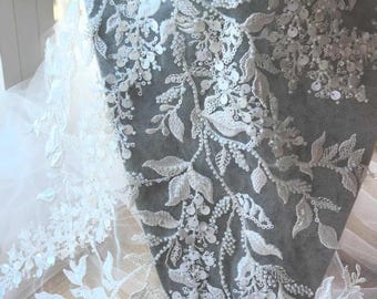 May include: White beaded lace fabric with a floral design. The fabric is delicate and intricate, with small white beads and sequins.