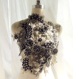 May include: Black and gold floral applique with beaded accents. The applique is made of lace and features a variety of flower shapes and sizes. It is perfect for adding a touch of elegance to any garment or project.