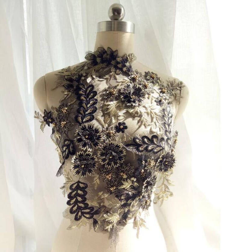 May include: Black and gold floral applique with beaded accents. The applique is made of lace and features a variety of flower shapes and sizes. It is perfect for adding a touch of elegance to any garment or project.