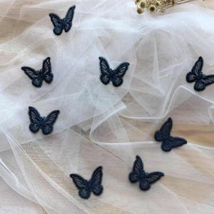 May include: A collection of eight black butterfly appliques on a white tulle fabric background.