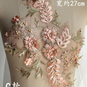 May include: A delicate floral applique with pink and gold embroidery on a sheer mesh fabric. The applique features intricate floral designs with pearl accents. The applique measures approximately 45 cm in height and 27 cm in width.