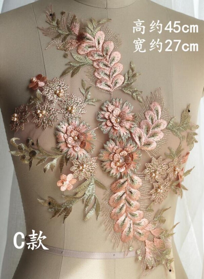 May include: A delicate floral applique with pink and gold embroidery on a sheer mesh fabric. The applique features intricate floral designs with pearl accents. The applique measures approximately 45 cm in height and 27 cm in width.
