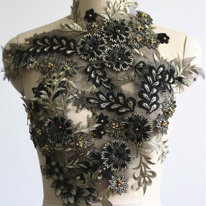 May include: Black and gold floral applique with beaded accents. The applique features a delicate floral design with intricate details. This applique is perfect for adding a touch of elegance to any garment or project.