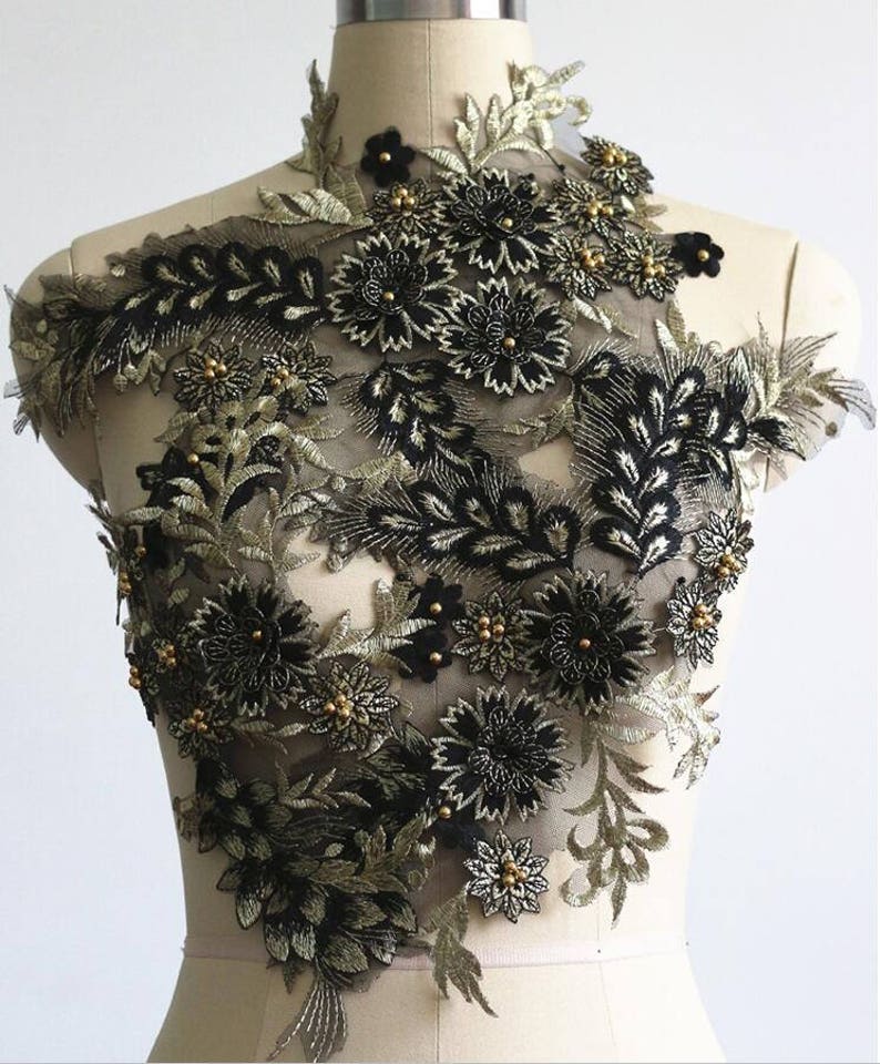 May include: Black and gold floral applique with beaded accents. The applique features a delicate floral design with intricate details. This applique is perfect for adding a touch of elegance to any garment or project.