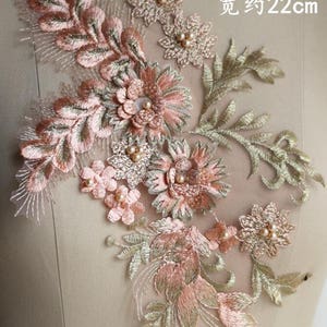May include: A delicate floral applique with pink and gold embroidery. The applique features a cluster of flowers and leaves, with pearl beads for embellishment. The applique measures approximately 39 inches tall and 22 inches wide.