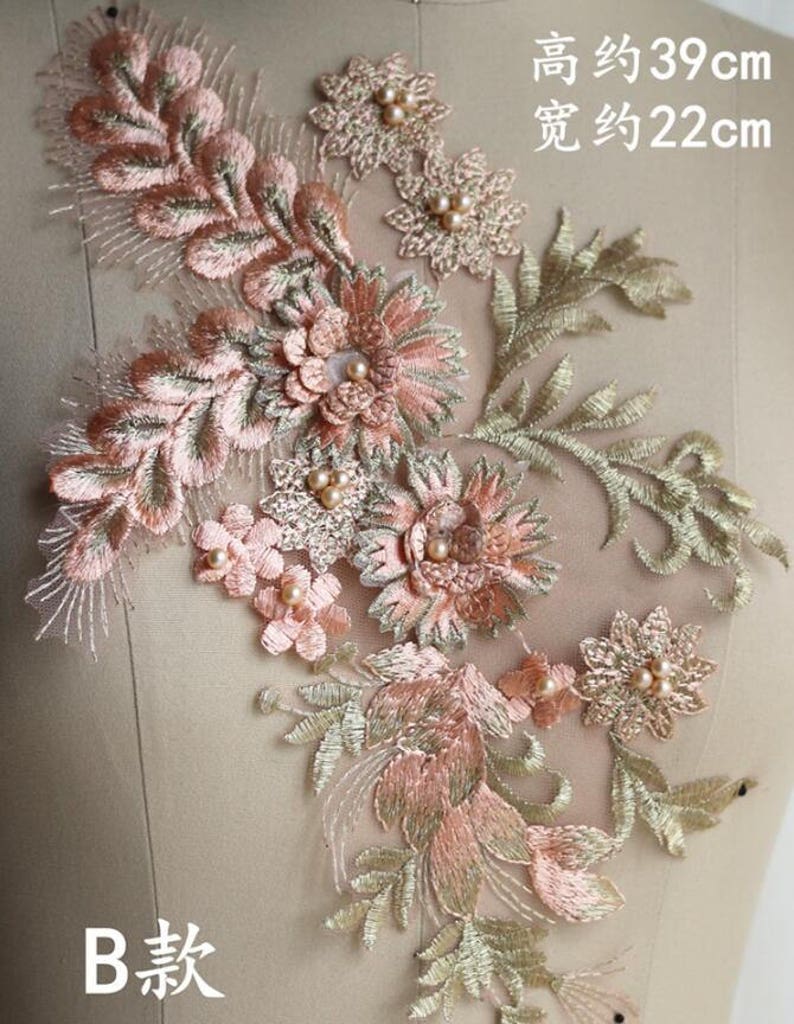 May include: A delicate floral applique with pink and gold embroidery. The applique features a cluster of flowers and leaves, with pearl beads for embellishment. The applique measures approximately 39 inches tall and 22 inches wide.