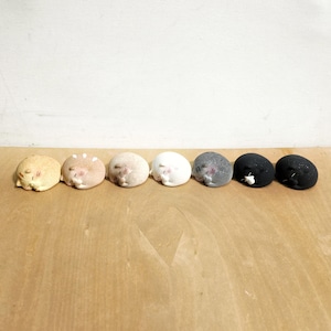Può includere: Un set di sette piccole statuette di gatti arrotondate in vari colori, tra cui crema, marrone chiaro, beige, bianco, grigio e due gatti neri. Ogni statuetta raffigura un gatto raggomitolato in posizione di riposo con occhi chiusi e orecchie.