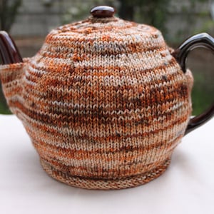 May include: A brown and white striped knitted teapot cosy. The cosy is made of a soft, textured yarn and has a classic design.