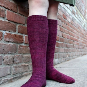 May include: A pair of long, maroon knee-high socks with a subtle marled texture. The socks are made of a soft, knitted fabric.