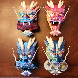 May include: Four dragon-shaped phone holders, each with a different color scheme. The holders are made of 3D printed plastic and feature a detailed dragon design with iridescent scales. The holders are designed to hold a smartphone in a vertical position.