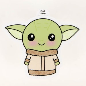 May include: A sticker with a cartoon illustration of a green alien character with large black eyes, rosy cheeks, and a smiling expression. The character wears a tan coat with a brown fur trim. The text "Peel Here" is at the top.