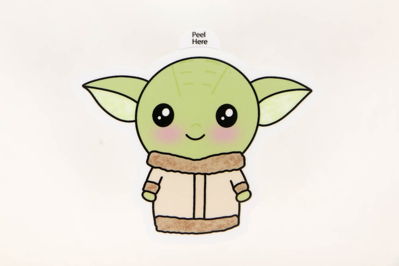 May include: A sticker with a cartoon illustration of a green alien character with large black eyes, rosy cheeks, and a smiling expression. The character wears a tan coat with a brown fur trim. The text "Peel Here" is at the top.
