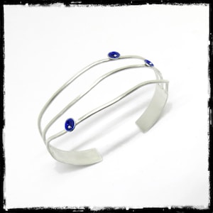 May include: A silver bangle bracelet with three bands and four blue enamel accents.