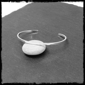 May include: A silver bangle bracelet with a hammered finish. The bracelet is open and has a simple, minimalist design.