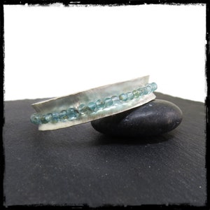 May include: A silver bangle bracelet with a row of light blue gemstone beads.