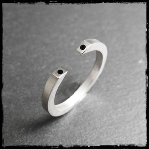 May include: A silver open circle bracelet with two black dots on the ends.