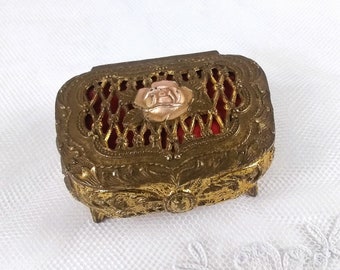 Beautiful little jewelry box with a rose on the lid! Footed gold tone box, the basket weave top is open and shows the red fabric inside.