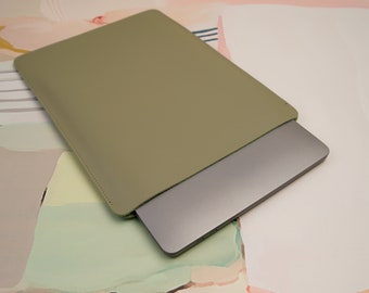 Può includere: Una custodia per laptop in pelle verde chiaro con un laptop argentato all'interno.