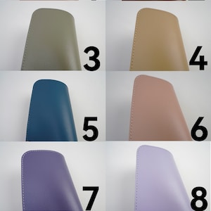 May include: Ten different colored leatherette cases for glasses or other small items. The cases are all the same size and shape, and they are arranged in two rows of five. The colors are brown, red, green, beige, blue, pink, purple, lavender, black, and white.