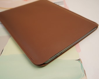 Può includere: Una custodia per laptop in pelle marrone con un bordo cucito.