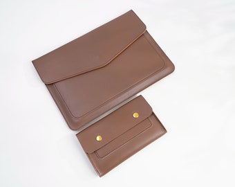 Può includere: Due pochette in pelle marrone con dettagli dorati. La pochette più grande è una custodia per laptop e la pochette più piccola è un portafoglio.