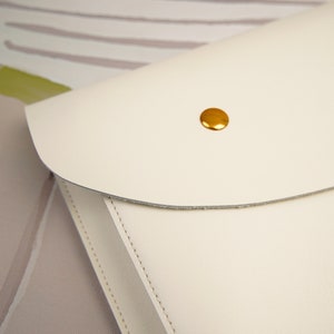 May include: A white leather clutch with a gold button closure.