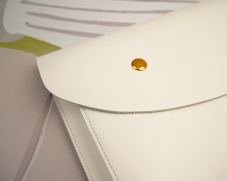 May include: A white leather clutch with a gold button closure.