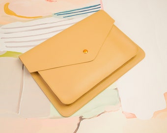 Può includere: Una pochette a busta in pelle beige chiaro con chiusura a bottone dorata.