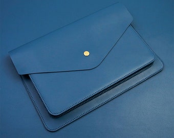 Può includere: Una custodia per laptop in pelle blu con chiusura a bottone dorata.