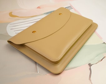 Può includere: Una pochette a busta in pelle color beige con chiusura a lembo e dettagli dorati. La pochette ha un design minimalista ed è perfetta per portare l'essenziale.