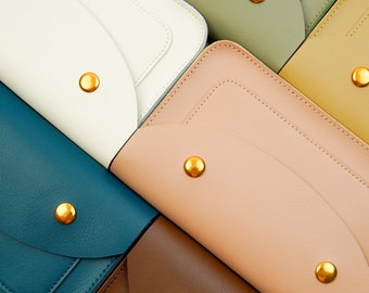 Può includere: Primo piano di sei portafogli in pelle di diversi colori, ognuno con una chiusura a bottone dorata. I portafogli sono disposti a ventaglio, con il portafoglio superiore di colore bianco, seguito da verde, beige, rosa, blu e marrone.