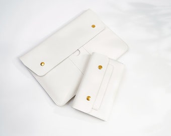 Può includere: Due buste in pelle bianca con chiusure in metallo dorato. La busta più grande ha una patta che si ripiega sul davanti. La busta più piccola è leggermente più piccola e ha un design simile.