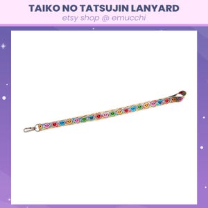 Puede incluir: Un cordón beige con un patrón repetido de caras sonrientes de colores. El cordón tiene un clip plateado en un extremo.