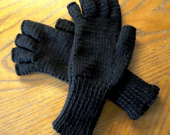 May include: A pair of black fingerless gloves, knitted with a ribbed cuff. The gloves are made of a dark, solid-colored yarn. The gloves are lying on a wooden surface.