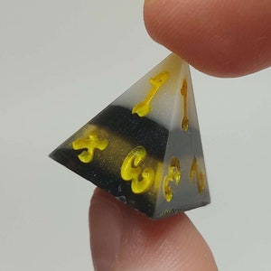 May include: A black, white, and yellow four-sided dice with yellow numbers.