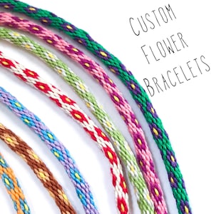 May include: Close-up of several colourful flower bracelets. The bracelets are woven with various colours, including green, pink, purple, red, and blue. The text "CUSTOM FLOWER BRACELETS" is written in black.