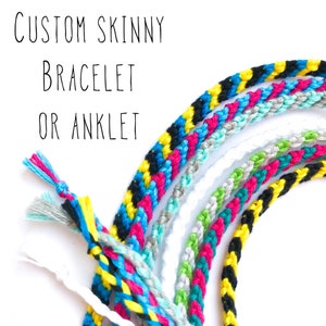 May include: A close-up of several colorful friendship bracelets and anklets made with braided string. The bracelets are in a rainbow of colors, including black, yellow, blue, pink, green, and white.