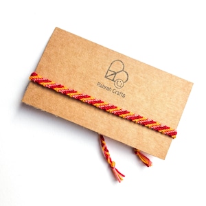 May include: A red, yellow and orange friendship bracelet with a brown card that says "Rahrah Crafts" and a logo of a heart with a smiley face inside.