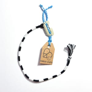 May include: A handmade bracelet with a black and white striped pattern. The bracelet is attached to a blue string and a small tag with the text "Rahrah Crafts". The bracelet is made of woven thread.