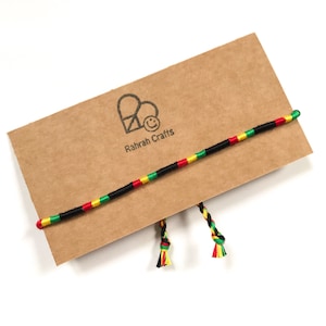 May include: A handmade bracelet with a black cord, featuring red, yellow, and green stripes. The bracelet is displayed on a brown card with the "Rahrah Crafts" logo. The ends of the bracelet have tassels in matching colors.