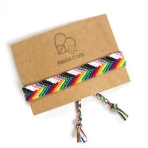 May include: A colorful friendship bracelet with a chevron pattern, displayed on a brown card. The bracelet features a variety of colors, including red, orange, yellow, green, blue, purple, black, white, and pink. The card has a logo that says "Rahrah Crafts".