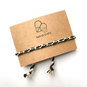 May include: A brown card with a black and white heart and smiley face logo that says "Rahrah Crafts". A black, white, and brown braided cord is wrapped around the card.