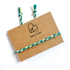 May include: A brown card with a green and white string tied around it. The card has a logo with a heart and a smiley face and the text "Rahrah Crafts".