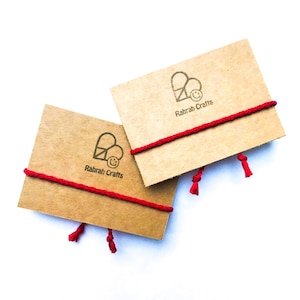 May include: Two brown cardboard gift tags with red string and tassels. Each tag has a logo with a heart and a smiley face and the text "Rahrah Crafts".